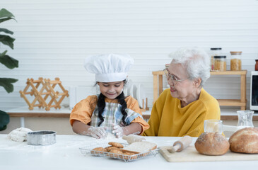 Happy family Asian elderly grandmother and little cute grandchild spend time together at kitchen, sift flour, knead dough and bake cookies or bread, smile and have fun, flour mess up on nose and face