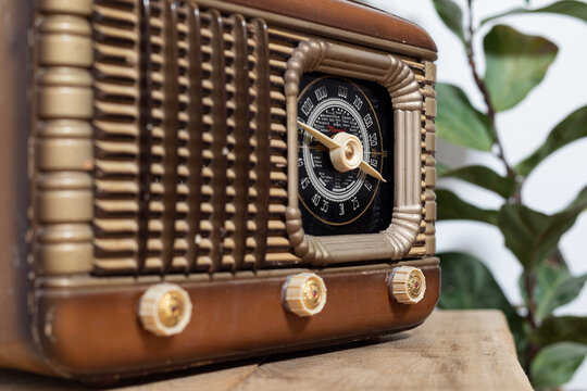 Closeup of an old fashioned radio, with dials and buttons, on a wooden table, with a plant in the background. Concept of listening to music. vintage radio