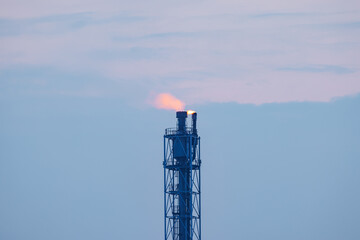 Close up of a candle tower with burning gas torch at oil refinery in morning time