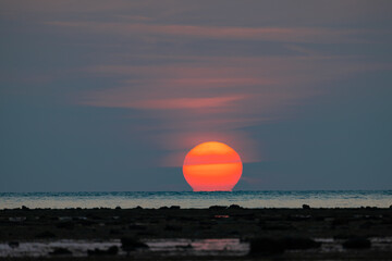 Beautiful omega sunset in the sea and beautiful orange sky with rock beach as foreground at Phuket, Southern of Thailand
