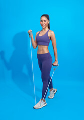 Fitness asian woman in sportswear exercising with a resistance band on blue background. Attractive active female doing squatting workout burning fat.