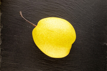 One sweet bright yellow pear on a slate stone, close-up, top view.