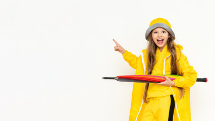 The child holds the umbrella horizontally, smiling broadly and pointing at your advertisement. A little girl in a yellow raincoat and a panama hat on a white isolated background. Copy Space.