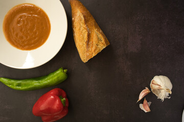 Andalusian gazpacho served in a white plate on a dark background. Tomato, pepper and fresh vegetable soup.