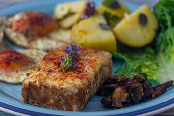 Fried tofu and eggs with lettuce and potatoes on blue circle dish and old table