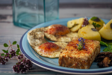 Fried tofu and eggs with lettuce and potatoes on blue circle dish and old table