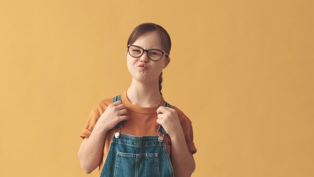 Medium portrait of pretty little girl with down syndrome smiling and making funny faces at camera standing on orange studio background