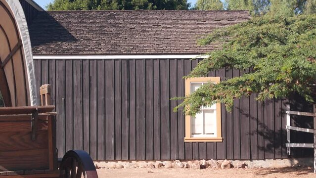 Old wooden retro covered wagon on wheels, wild west pioneer ranch. Western historic retro cart, traditional vintage transport. Rural house wall, building exterior. Countryside farm or cowboy saloon.