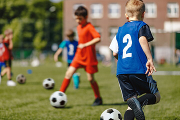 Football Summer Traing Camp For School Kids. Soccer Players Running Classic Soccer Ball on Natural Grass Field. Kids in Red and Blue Soccer Uniforms Playing Match