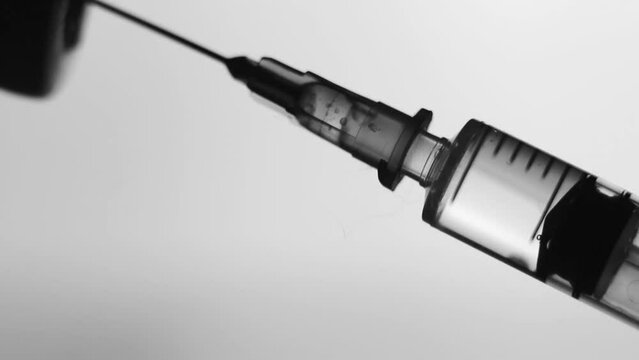 vaccination concept, syringe injected clear liquid in glass vial close up. drawing vaccine into a syringein bubbles inside. soft grey background. horizontal black and white slow motion macro HD video.