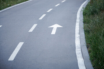 Fototapeta premium White arrow sign on the street. Directional arrow painted on pavement asphalt. Direction for traffic safety way. Symbol of crossroads. Pointer on gray asphalt floor.