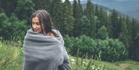 A young woman wrapped in a blanket in the mountains.