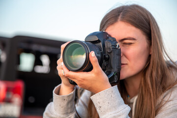 A young woman with a professional camera takes a photo in nature.