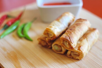 Fried chinese spring rolls with sweet chili sauce served on light wooden cutting boards and fresh chili.