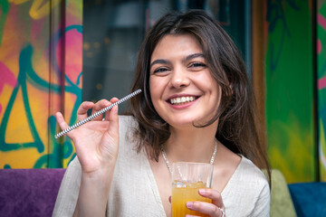 Happy young woman with a glass of lemonade against a bright painted wall.