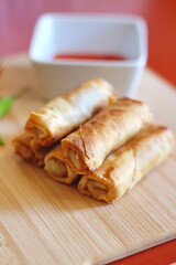 Fried chinese spring rolls with sweet chili sauce served on light wooden cutting boards and fresh chili.