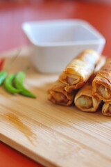 Fried chinese spring rolls with sweet chili sauce served on light wooden cutting boards and fresh chili.