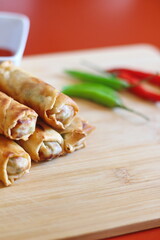 Fried chinese spring rolls with sweet chili sauce served on light wooden cutting boards and fresh chili.