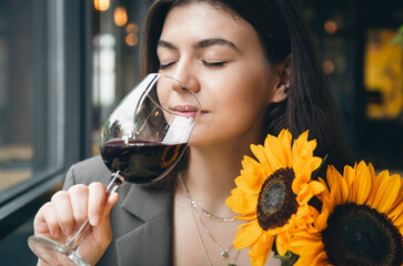 A young woman with a glass of wine and a bouquet of sunflowers in a restaurant.
