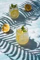 Homemade lemonade with lemon, mint and ice cubes in glasses on a light blue background. Cold summer refreshing drinks. Photo of lemonade with hard shadows.