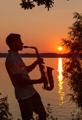 A young guy plays the saxophone in the evening at sunset