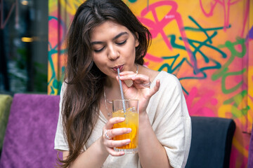 Happy young woman with a glass of lemonade against a bright painted wall.