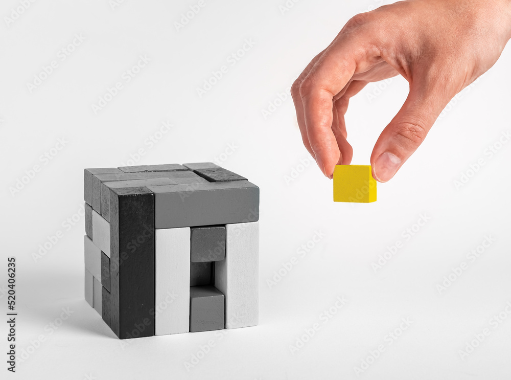 Poster hand putting last outstanding element in puzzle cube. yellow block in black and white construction. 