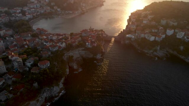 Drone orbit around island and Amasra city in Turkey northern province Bartin. Sun shine on sea surface through old Kemere Bridge during sunset