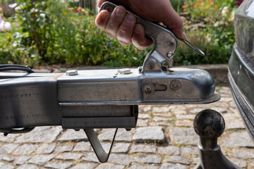 man's hand checks the fixation of the trailer closed hitch lock handle on the towing ball towbar of the car closeup, the safety of driving with a trailer on the road