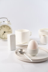 White egg with white plates, cup and alarm clock over white background for breakfast