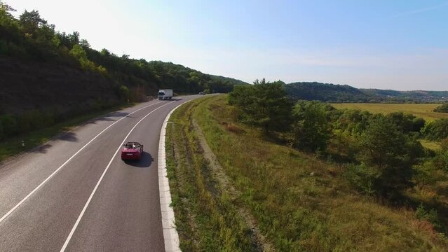 Aerial View Of Couple Driving Red Convertible Sports Car Down Country Road.