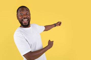 Excited Black Man Pointing Fingers Aside Over Yellow Studio Background