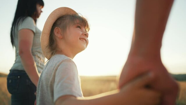 Happy family. Child walks with his parents by the hand. Child care. Cheerful smile on child's face. Family walk in the meadow in nature. Sun rays on the face. Happy family and active lifestyle concept