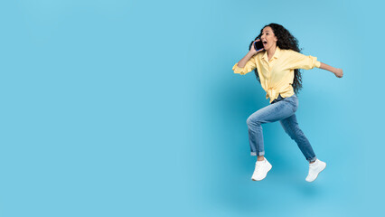 Fototapeta na wymiar Woman Talking On Phone Running In Mid Air, Blue Background
