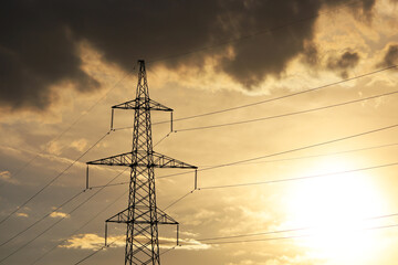 Silhouette of high voltage tower with electrical wires on background of sunset sky and dark clouds....