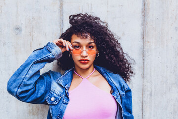 closeup portrait of teen woman wearing orange glasses and blue jacket posing in city trendy looking...