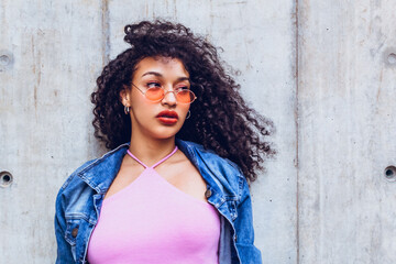 closeup portrait of teen woman wearing orange glasses and blue jacket posing in city trendy looking on isolated gray background, generation z woman in city, urban concept.