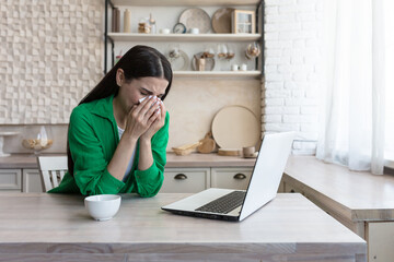 Online consultation with a family psychologist, a young beautiful woman in the kitchen cries in depression, uses a laptop for a video call, consults with a psychotherapist