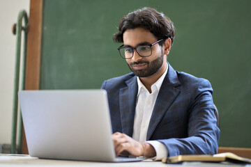 Young indian business man executive wearing suit working on laptop sitting in office at work desk....