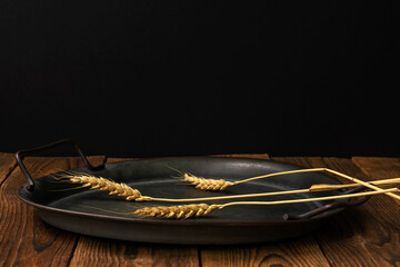 Three spikelets of ripe wheat lie on a rustic plate on an old wooden table. Country style. Black background. Meager and poor food. High quality. low key