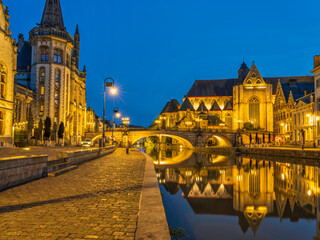 Naklejka premium Historic medieval building and Arched stone bridge illuminated at night on Leie river in Ghent, Belgium