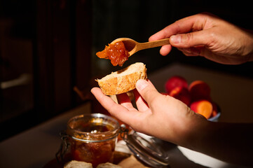 Food and drink, summer autumn harvest concept. Cropped view of the hands of a housewife spreading apricot jam on bread