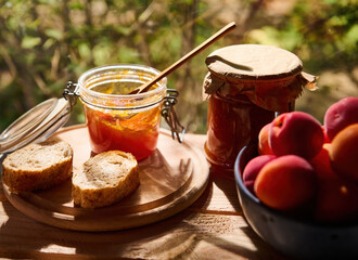 Still life of a homemade apricot confiture, sliced bread and delicious ripe fruits on wooden table, in nature background