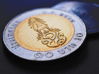 Translation: 10 baht Thailand. Thai coin lies on dark surface close up. News about money or...