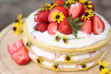 tiered layered cake with yellow wildflowers and strawberries with white frosting icing on wood board summer cake rustic minimalist - naked cake