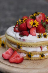 tiered layered cake with yellow wildflowers and strawberries with white frosting icing on wood board summer cake rustic minimalist - naked cake