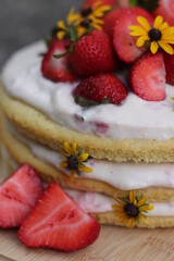 tiered layered cake with yellow wildflowers and strawberries with white frosting icing on wood board summer cake rustic minimalist - naked cake