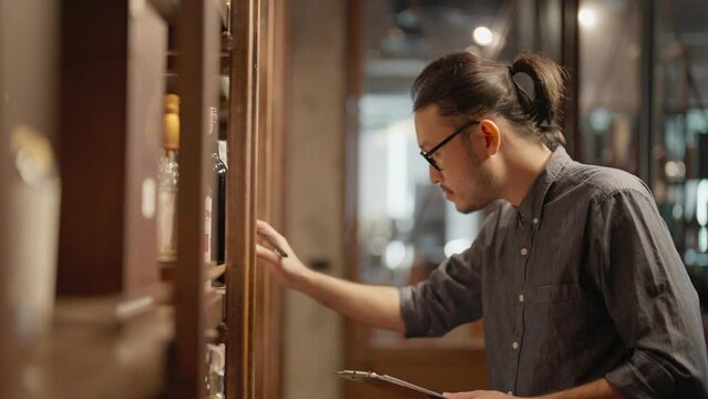 A male bartender is using a tablet to check product in a store. He checking wine label at wine store.