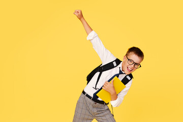 School break. Cheerful mischievous schoolboy in uniform with a backpack jumps on a yellow...