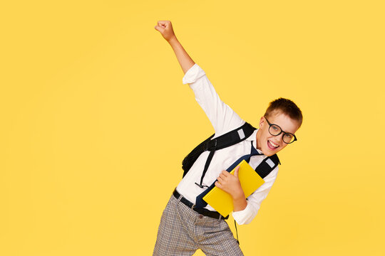 School break. Cheerful mischievous schoolboy in uniform with a backpack jumps on a yellow background. Beginning of holidays. Back to school.